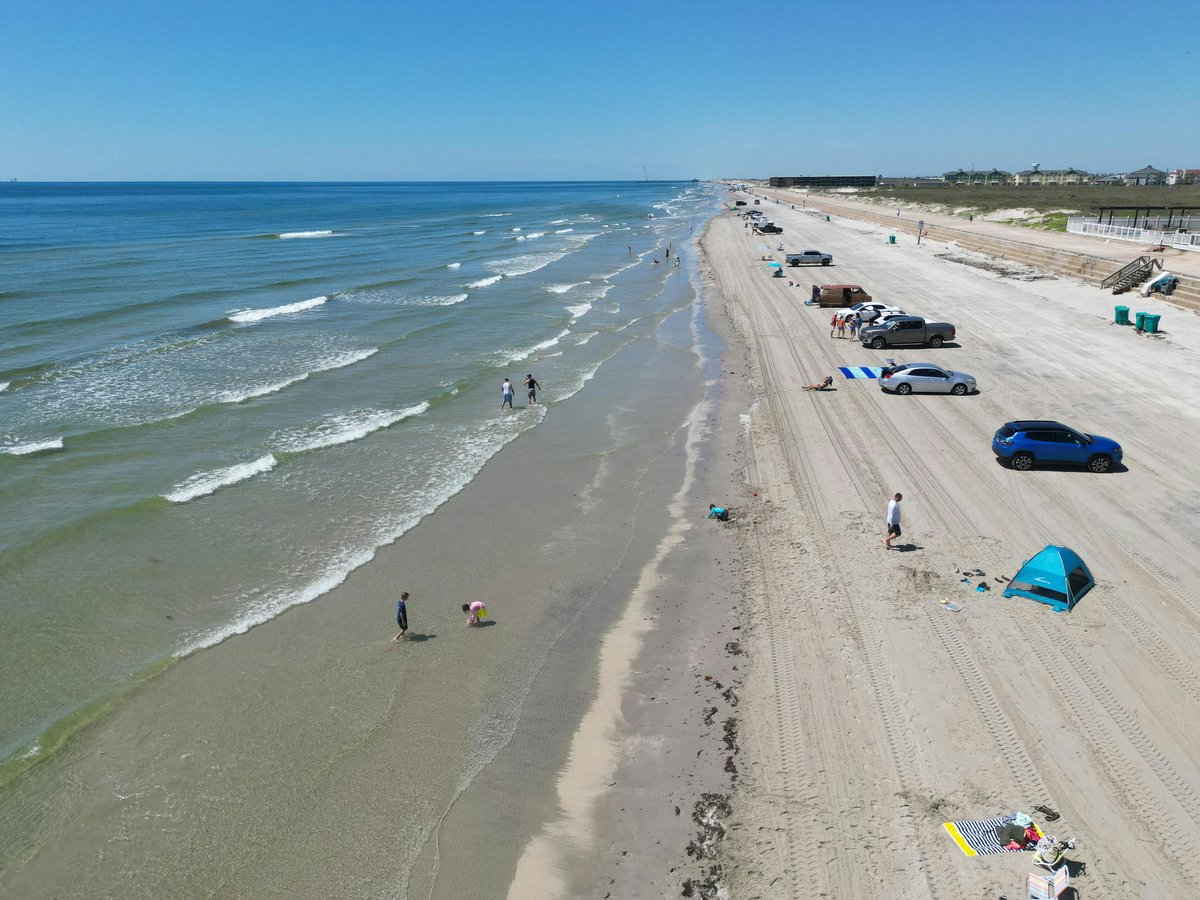Serene aerial view of a sunny day on North Padre Island beach, Texas with cars and people enjoying the shoreline.