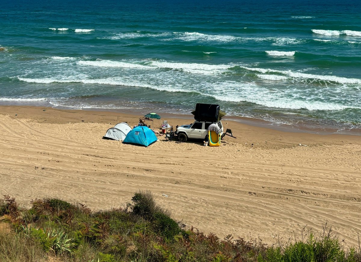Tents and SUV on a scenic sandy beach with ocean waves, perfect for a beach camping adventure.