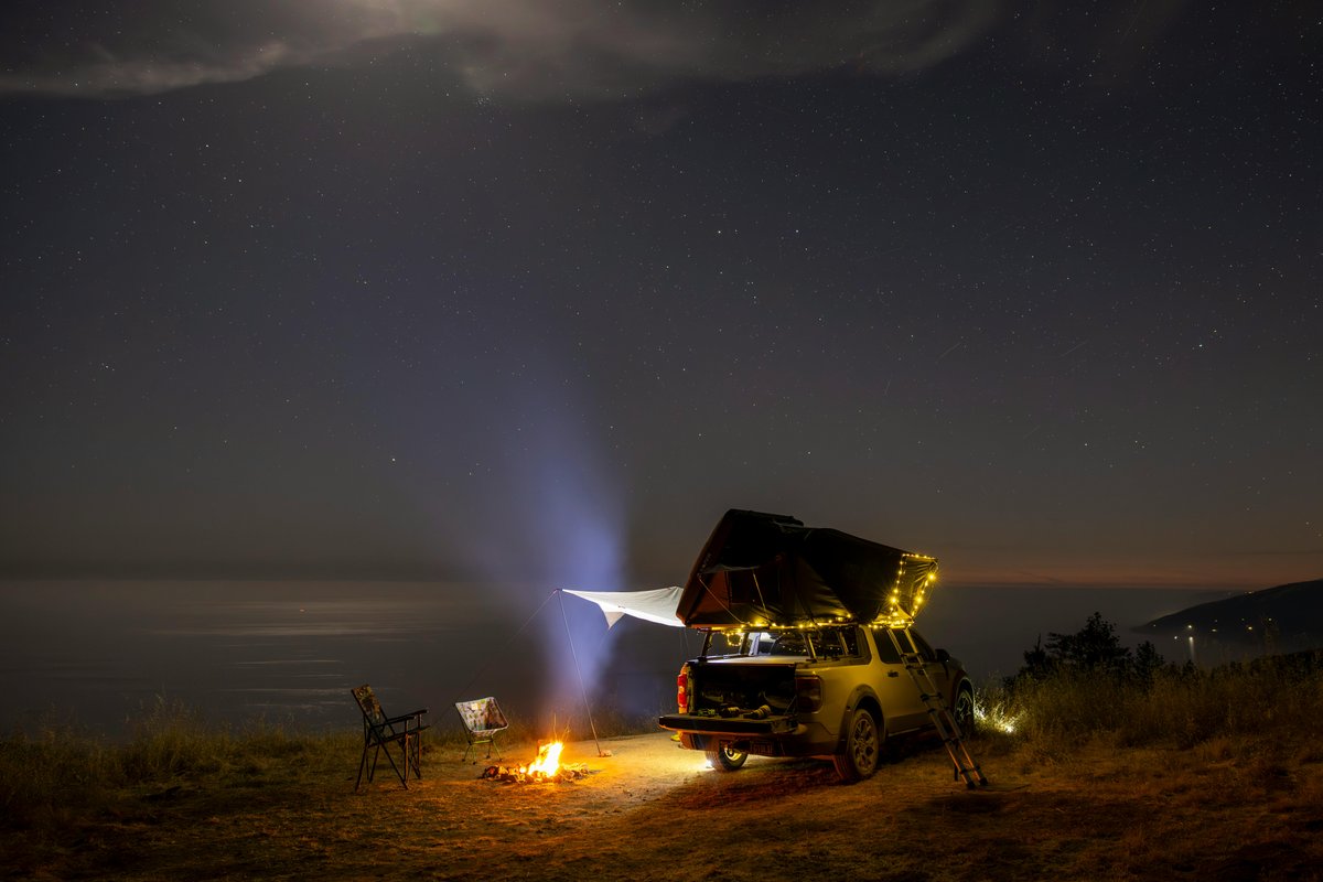 A peaceful camping setup with a vehicle and campfire under a starlit sky, offering a serene outdoor experience.